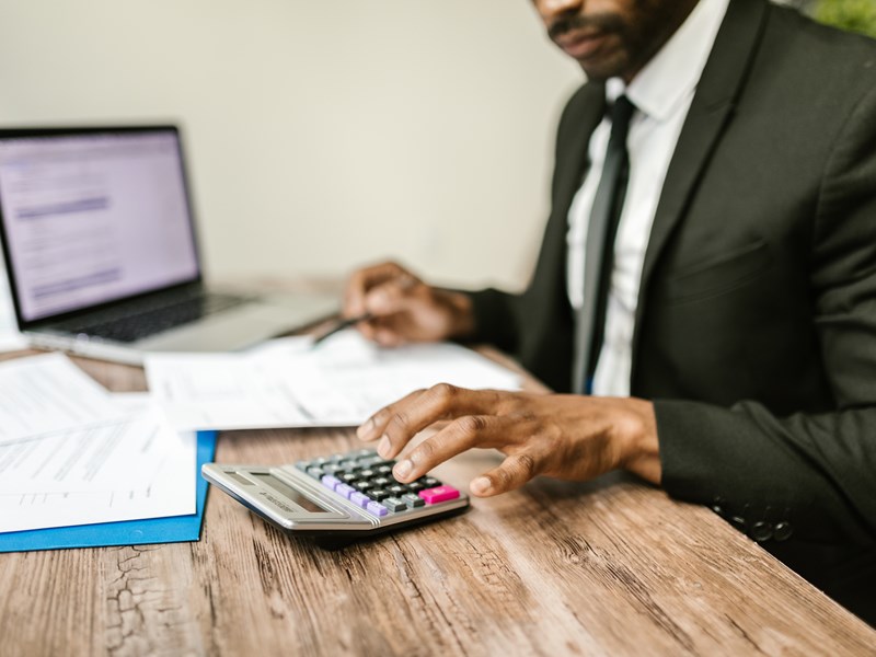 A man in a suit using a calculator at his desk to help him with his work.