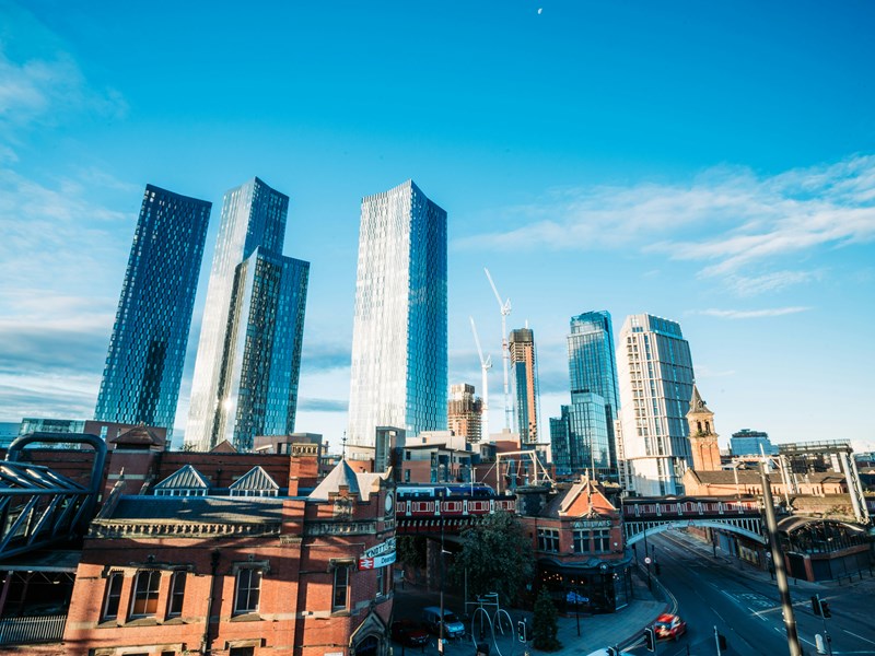 Image of Manchester city centre skyline, showing skyscraper buildings and a blue sky.
