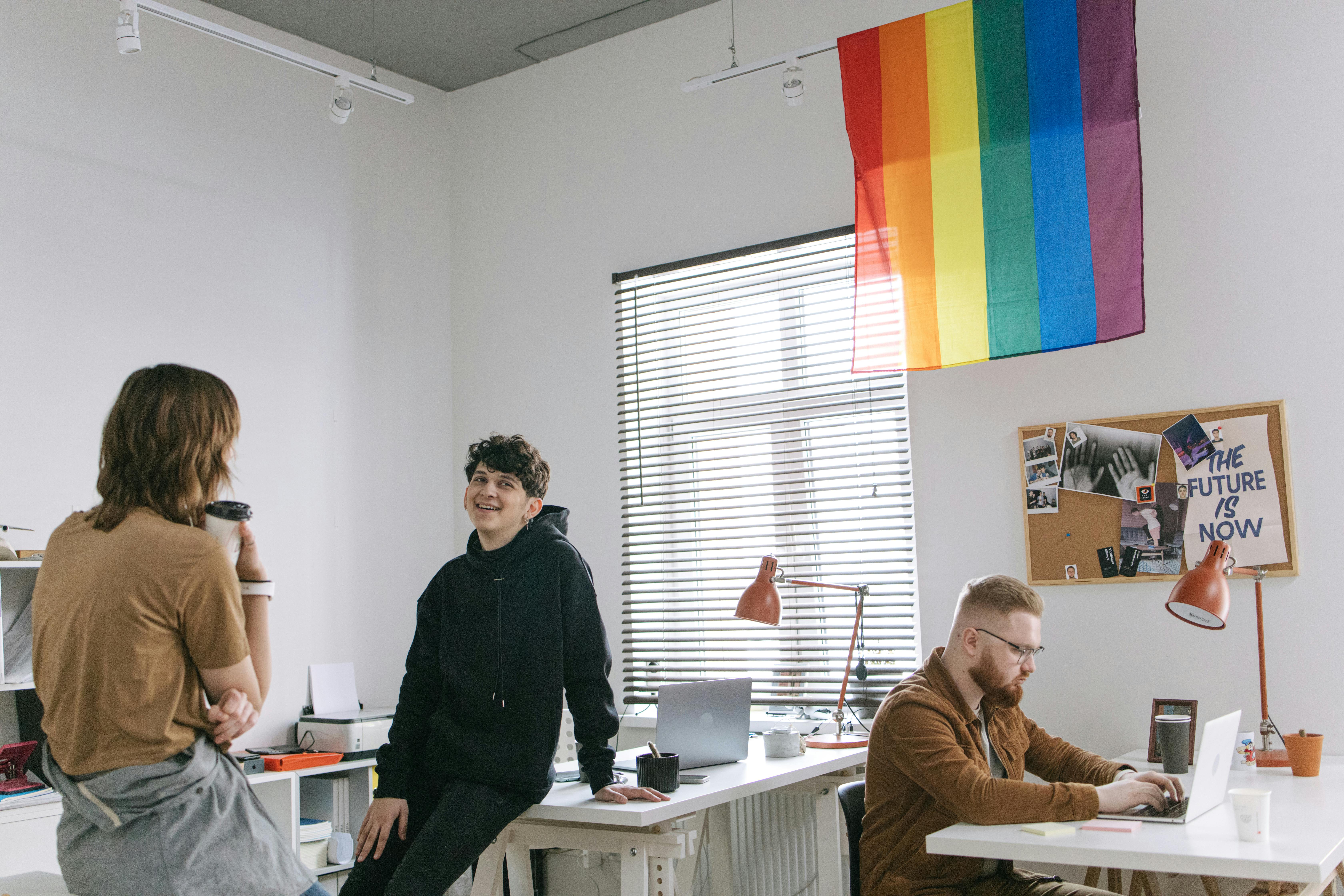 People sat talking in an office. An LGBT flag is draped from the ceiling.