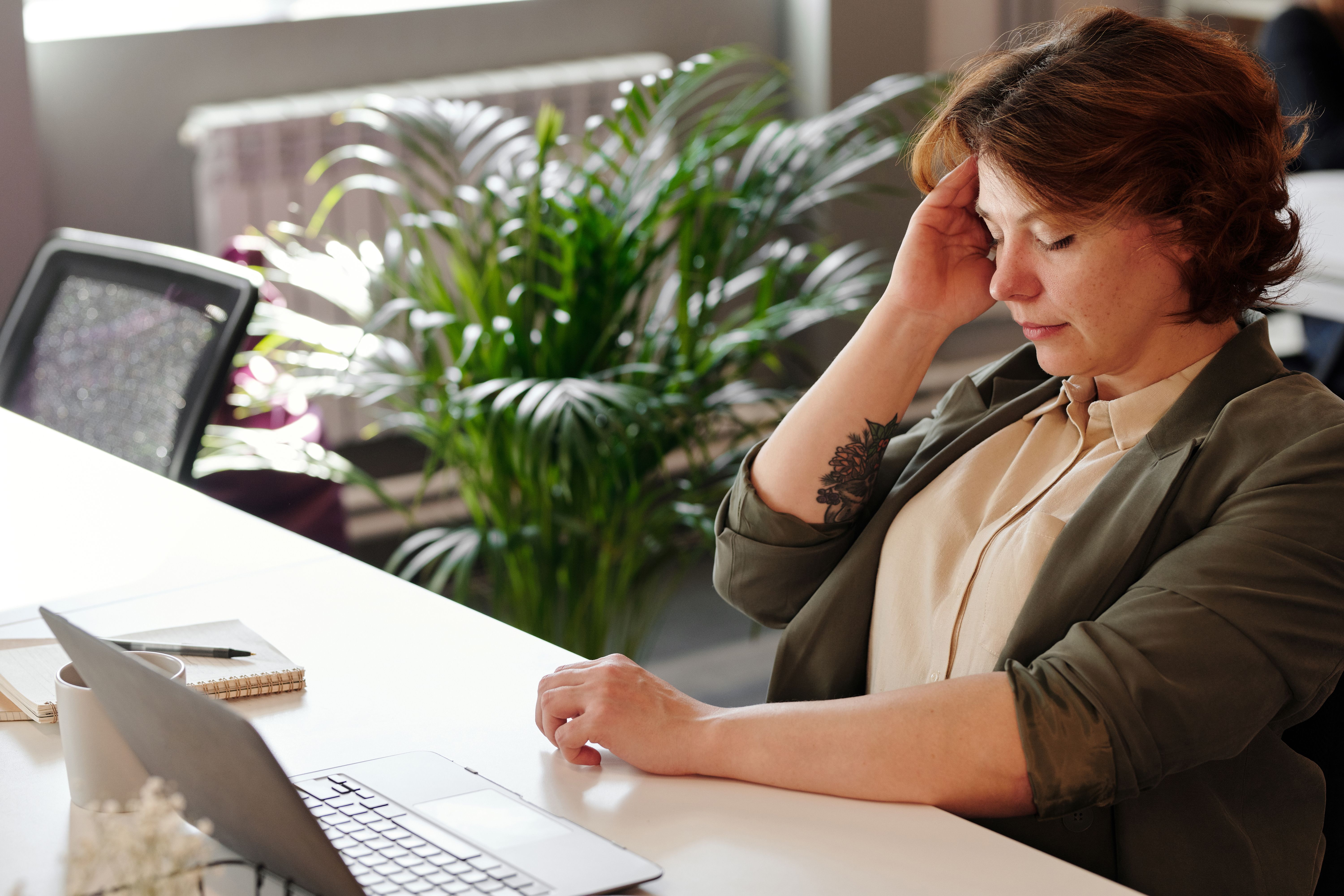Lady struggling at her work desk, hand on head.